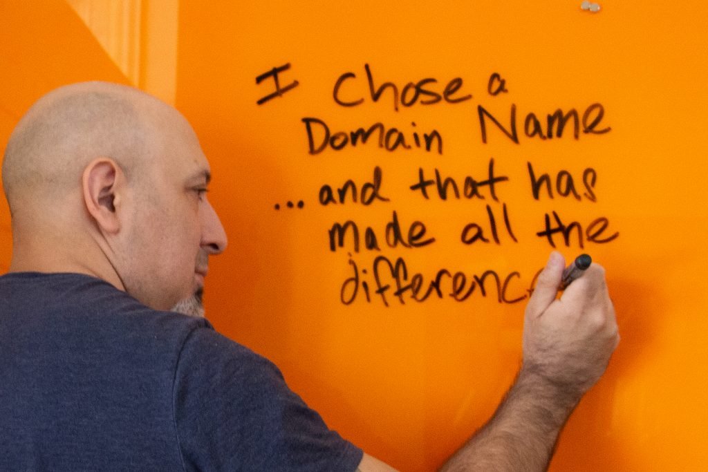 Jason Orellana writing on orange board. Text: I chose a domain name…and that has made all the difference